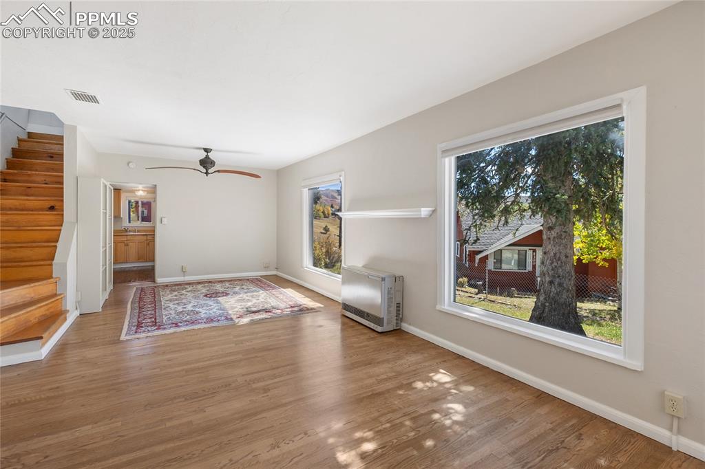 Unfurnished living room with stairway, wood finished floors, heating unit, and ceiling fan