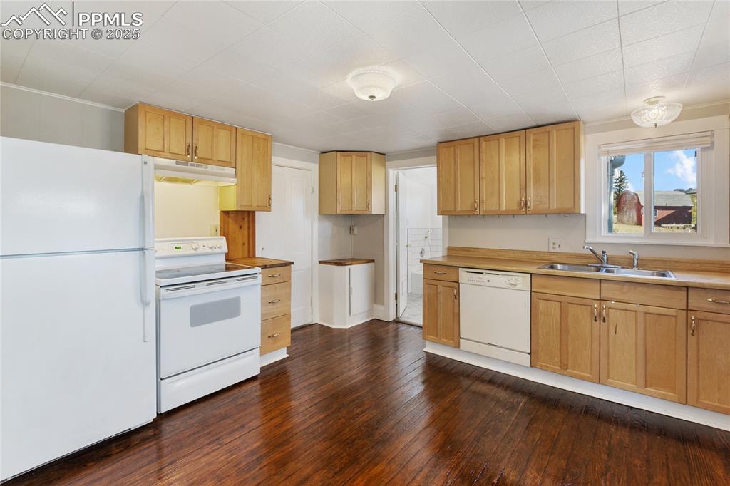 Kitchen featuring white appliances, dark wood-style flooring, light countertops, light brown cabinetry, and under cabinet range hood