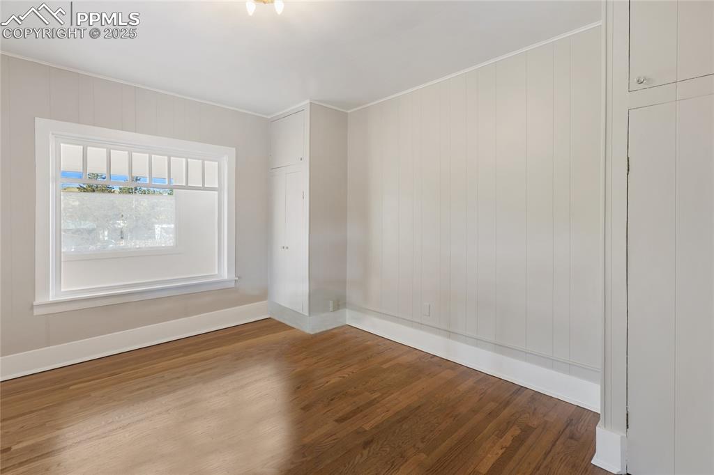Empty room featuring wood finished floors, wooden walls, and ornamental molding