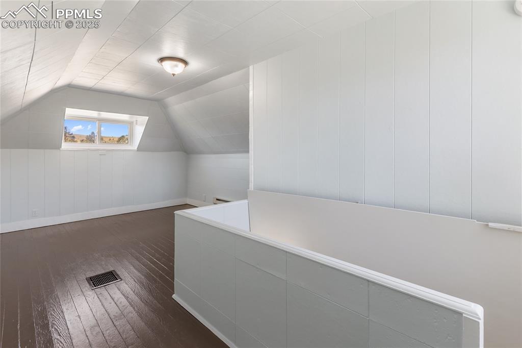 Bonus room with vaulted ceiling, dark wood-type flooring, and wood walls