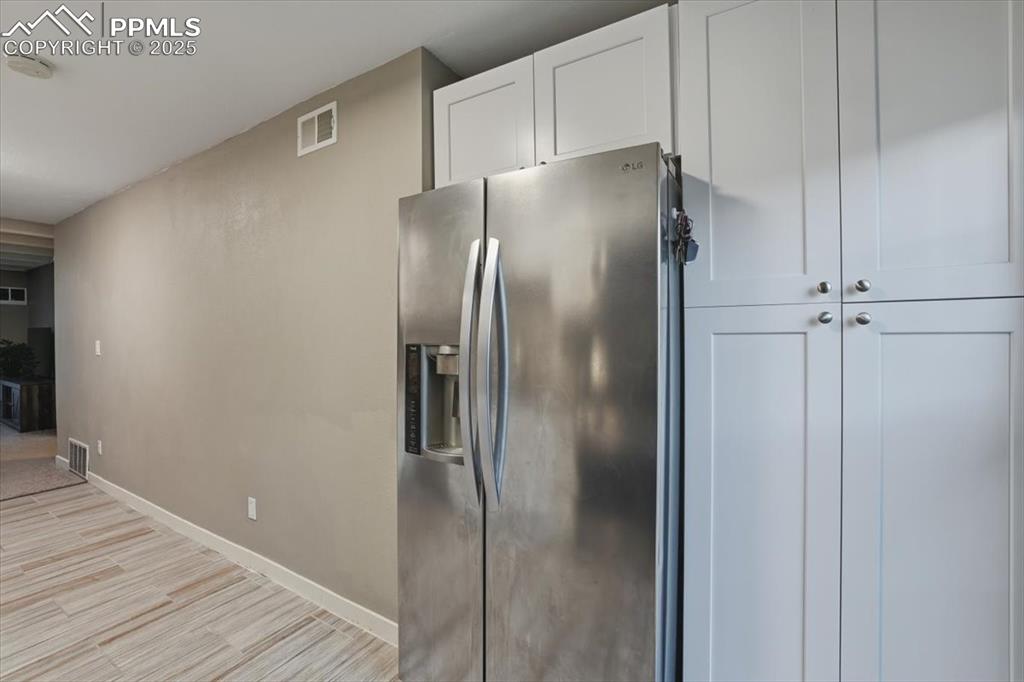 Kitchen with stainless steel fridge, light wood-style floors, and white cabinetry