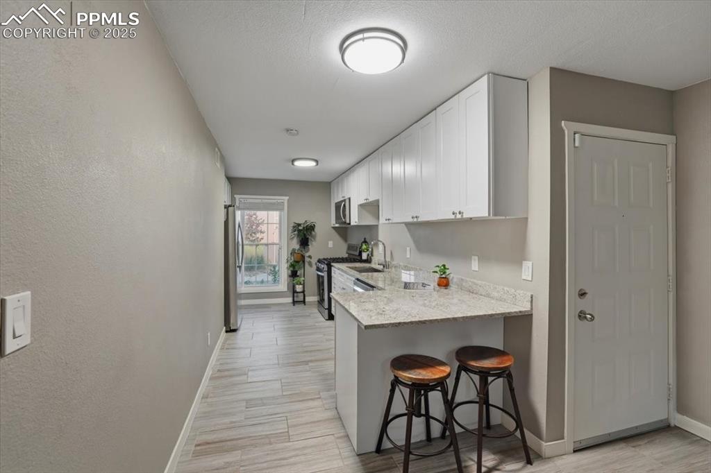 Kitchen with a breakfast bar area, white cabinets, wood tiled floors, stainless steel appliances, and a peninsula