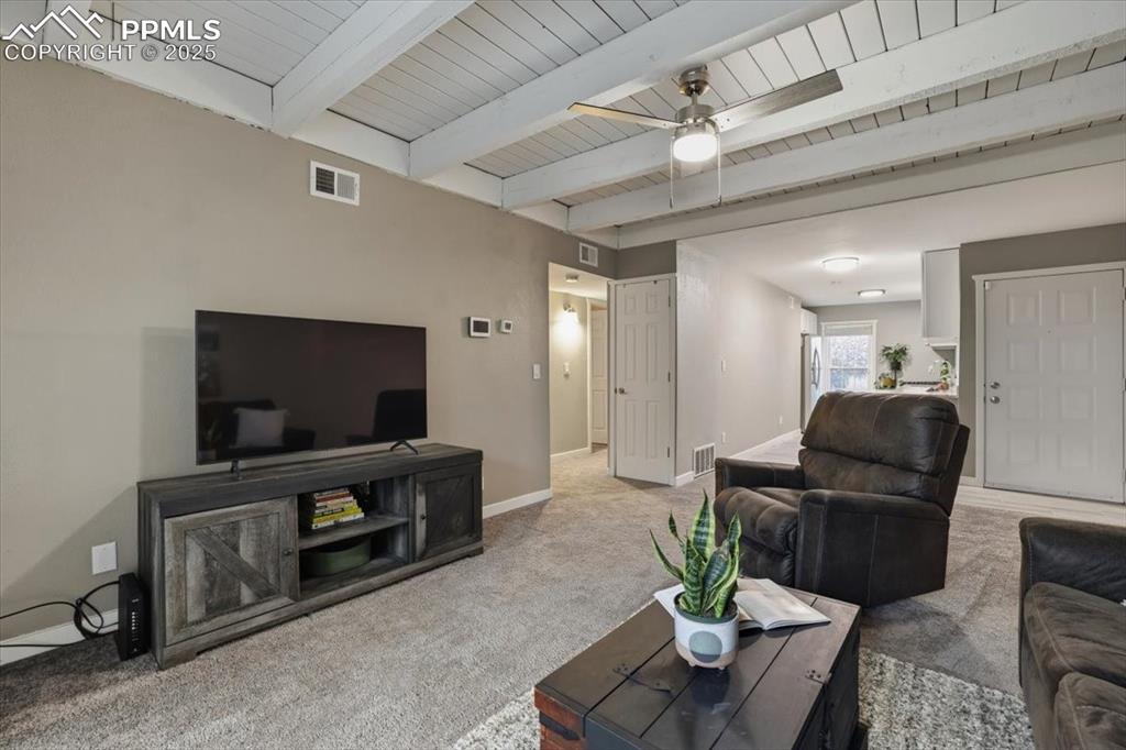 Carpeted living room featuring a ceiling fan and a wooden ceiling with exposed beams