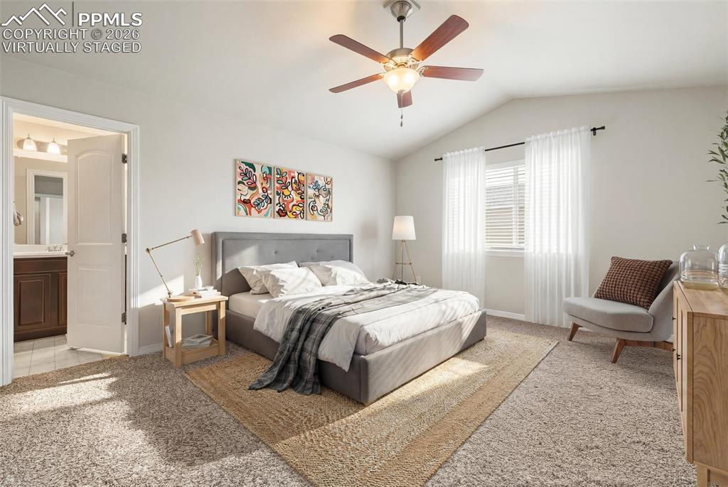 Bedroom featuring light carpet, ceiling fan, lofted ceiling, and connected bathroom. Virtually staged.
