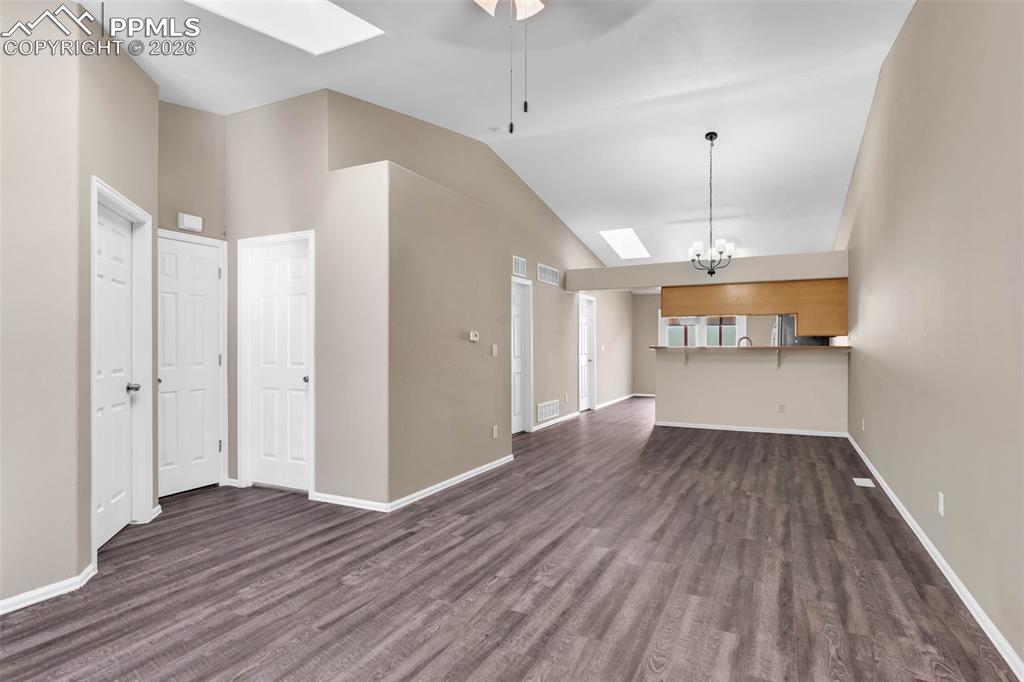 Unfurnished living room featuring a skylight, vaulted ceiling, dark wood-type flooring, hanging lights, and a ceiling fan