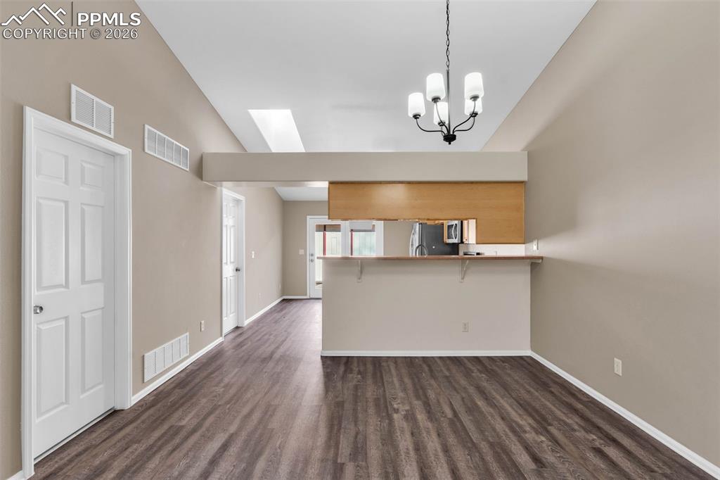 Unfurnished dining area featuring vaulted ceiling, a skylight, dark wood-type flooring, and a chandelier