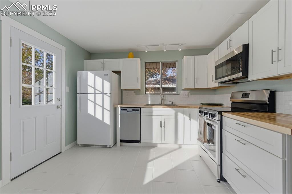 Kitchen with stainless steel appliances, backsplash, white cabinets, and ceramic patterned floors
