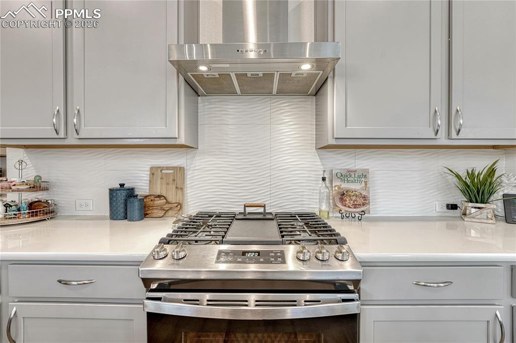 Beautiful full height, white backsplash and a full gas range, center griddle and stainless kitchen vent fan
