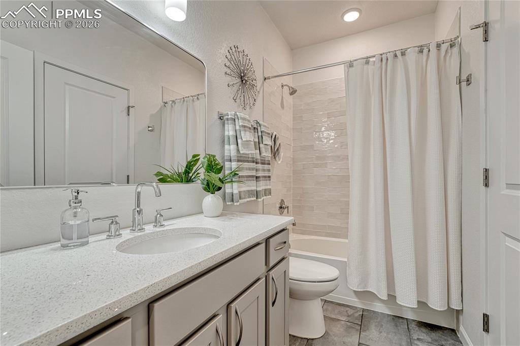 The upper-level full bathroom has sparkling white quartz counters and a textured tile shower / tub surround
