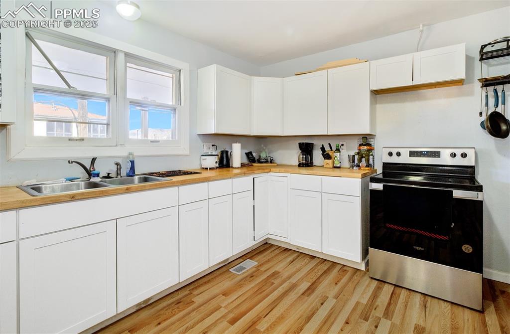 Kitchen featuring white cabinetry, electric range, a sink, light wood-style floors, and visible vents