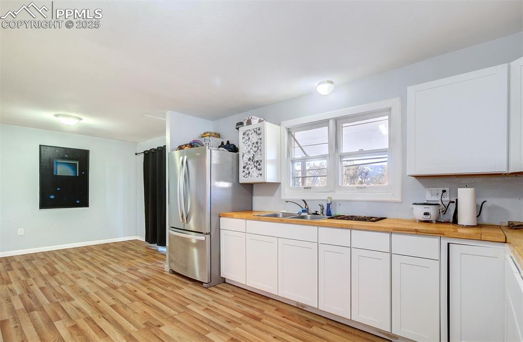 Kitchen with wood counters, white cabinetry, a sink, light wood-style floors, and freestanding refrigerator