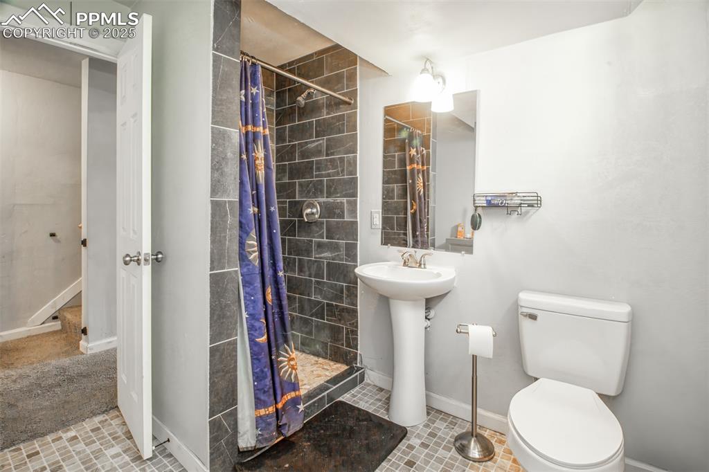 Full bath featuring baseboards, a tile shower, toilet, and a sink