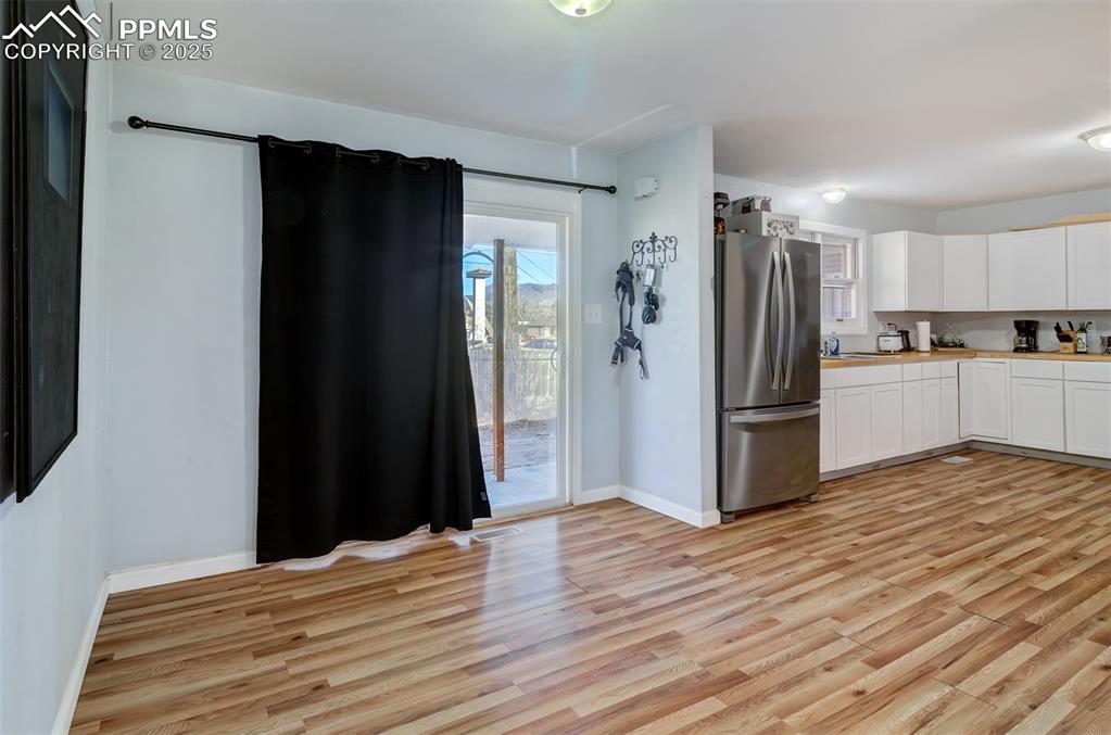 Kitchen with light countertops, light wood finished floors, baseboards, white cabinetry, and freestanding refrigerator