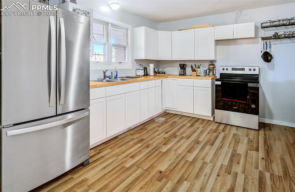Kitchen with white cabinetry, butcher block countertops, stainless steel appliances, a sink, and light wood-style flooring