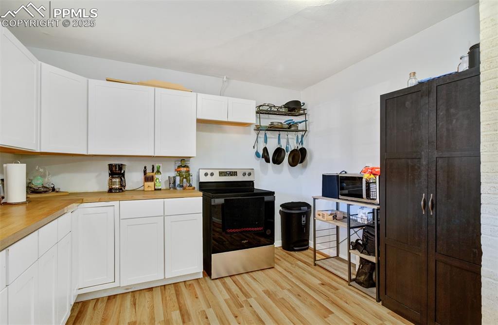 Kitchen with white cabinets, wooden counters, stainless steel range with electric cooktop, and light wood-type flooring