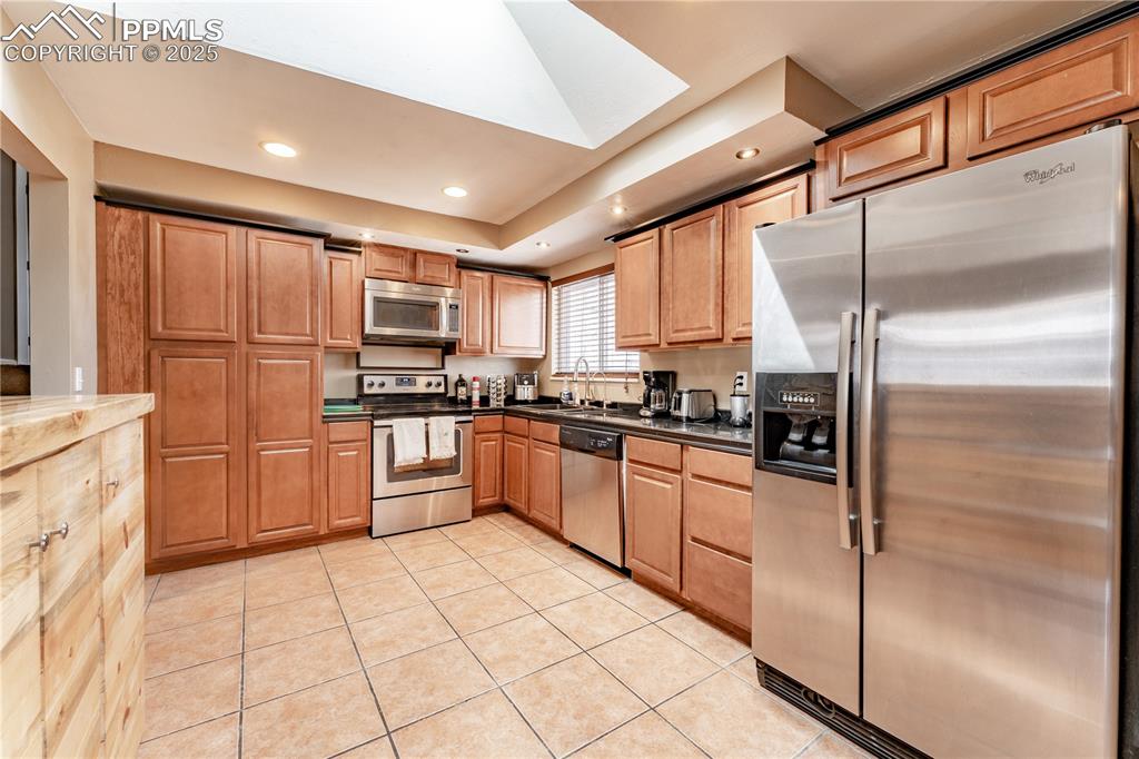 Kitchen featuring stainless steel appliances, light tile patterned floors, recessed lighting, a skylight, and dark countertops