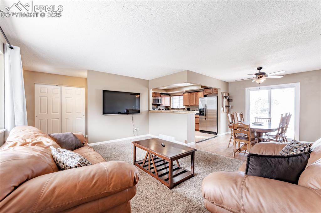 Living room with a ceiling fan, a textured ceiling, and light tile patterned floors