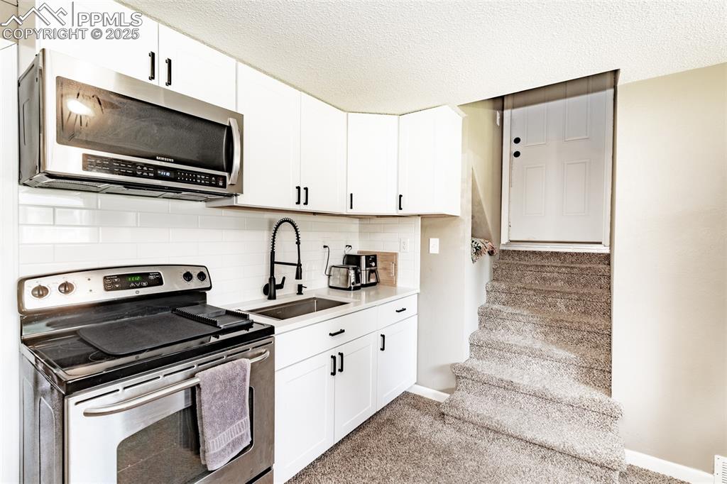 Kitchen with appliances with stainless steel finishes, white cabinets, decorative backsplash, and a textured ceiling