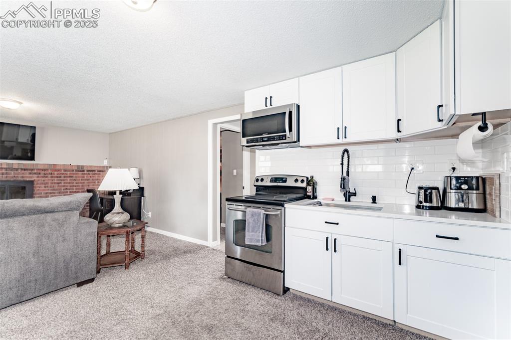 Kitchen featuring stainless steel appliances, white cabinets, a textured ceiling, light carpet, and backsplash