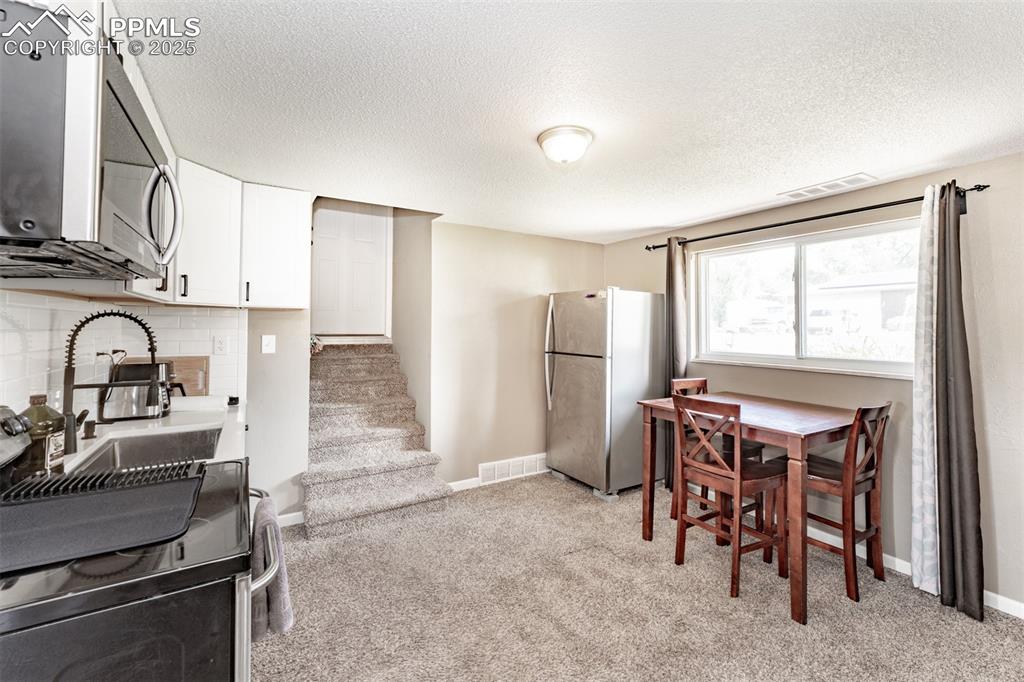 Kitchen featuring appliances with stainless steel finishes, light colored carpet, backsplash, white cabinetry, and a textured ceiling