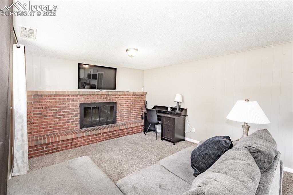 Carpeted living room with a brick fireplace, a textured ceiling, and an office area