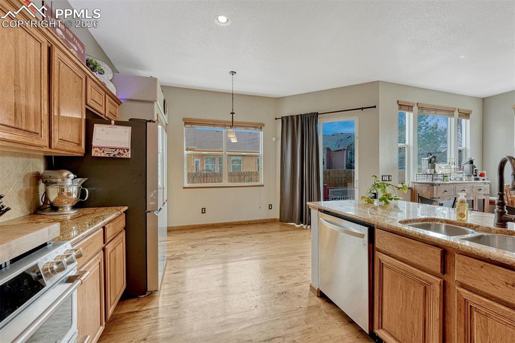 Kitchen with light stone countertops, stainless steel appliances, pendant lighting, and light wood-style flooring