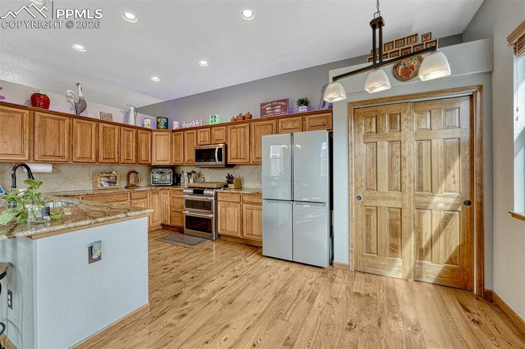 Kitchen with stainless steel appliances, light stone counters, light wood finished floors, wood finish cabinets, and decorative light fixtures