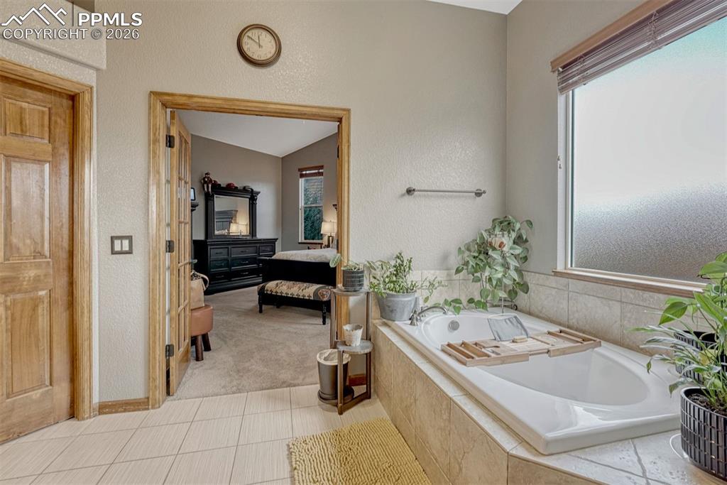 Primary bathroom. Bathtub, vaulted ceiling, light tile floors, Shower