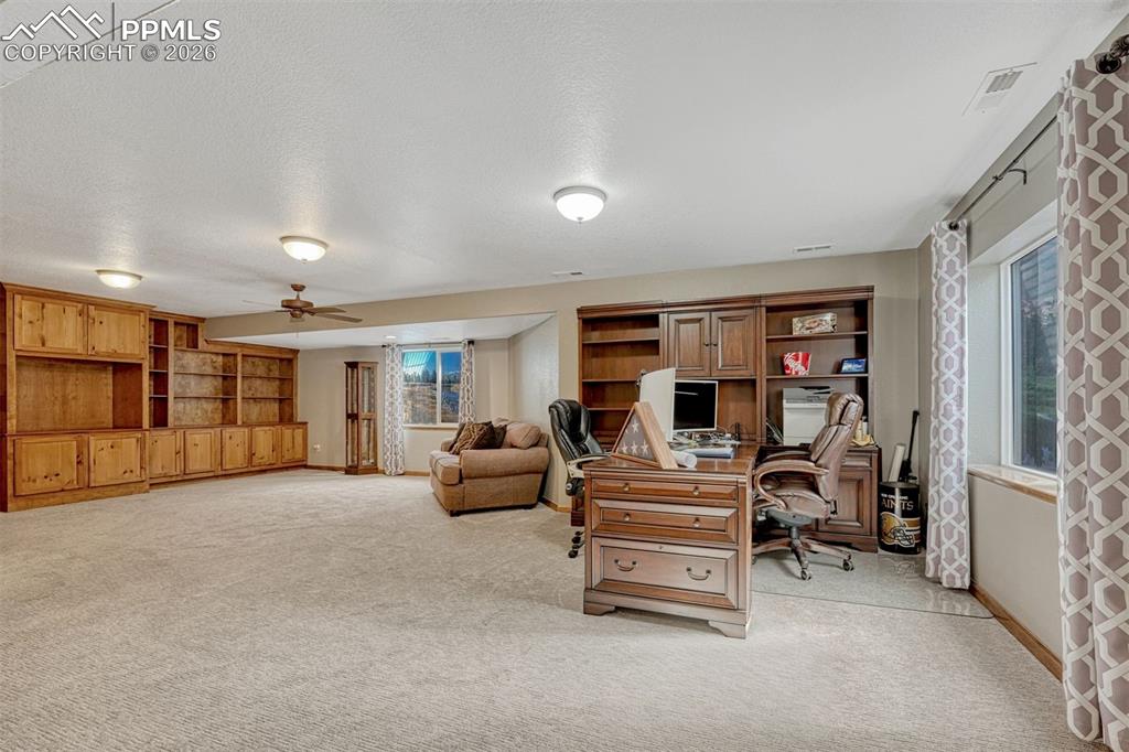 Office set up in the basement with ceiling fan, light carpet, and a textured ceiling