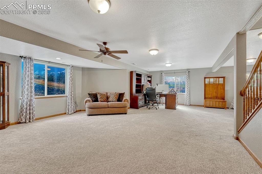 Living room featuring a desk, light colored carpet, a textured ceiling, and a ceiling fan