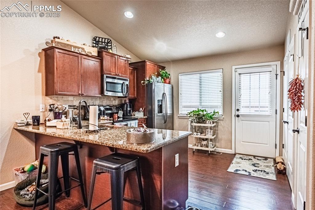 Kitchen featuring a textured wall, a peninsula, light stone counters, stainless steel appliances, and a kitchen breakfast bar