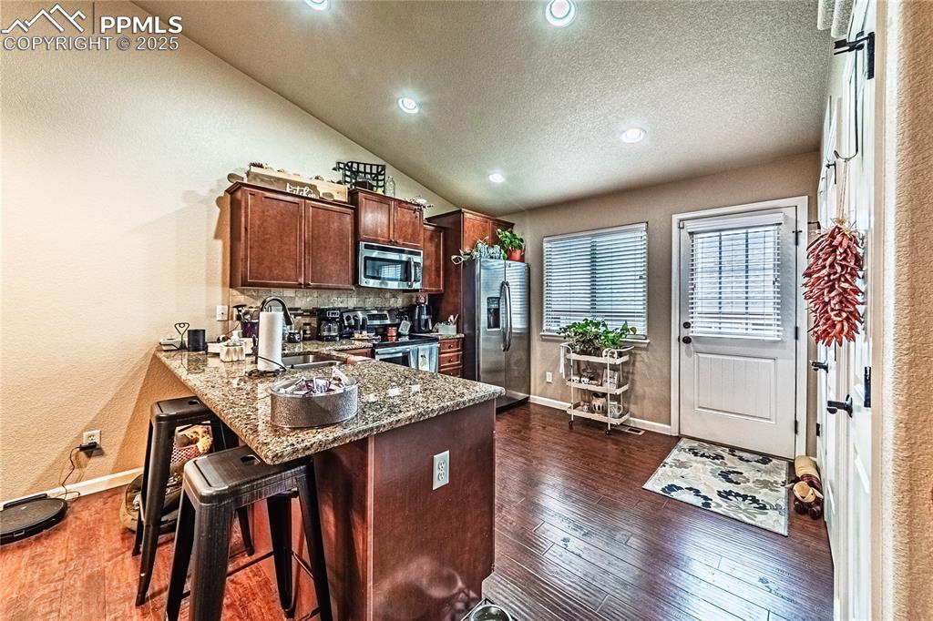 Kitchen with dark stone counters, vaulted ceiling, a peninsula, a breakfast bar, and dark wood-type flooring