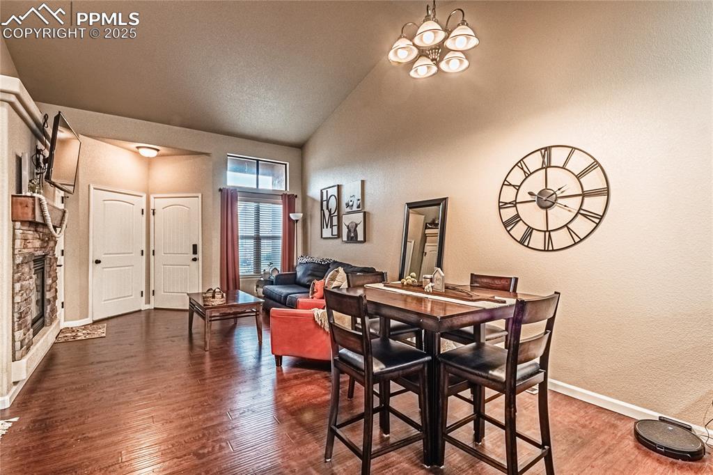 Dining space featuring wood finished floors, a textured wall, a chandelier, a fireplace, and high vaulted ceiling