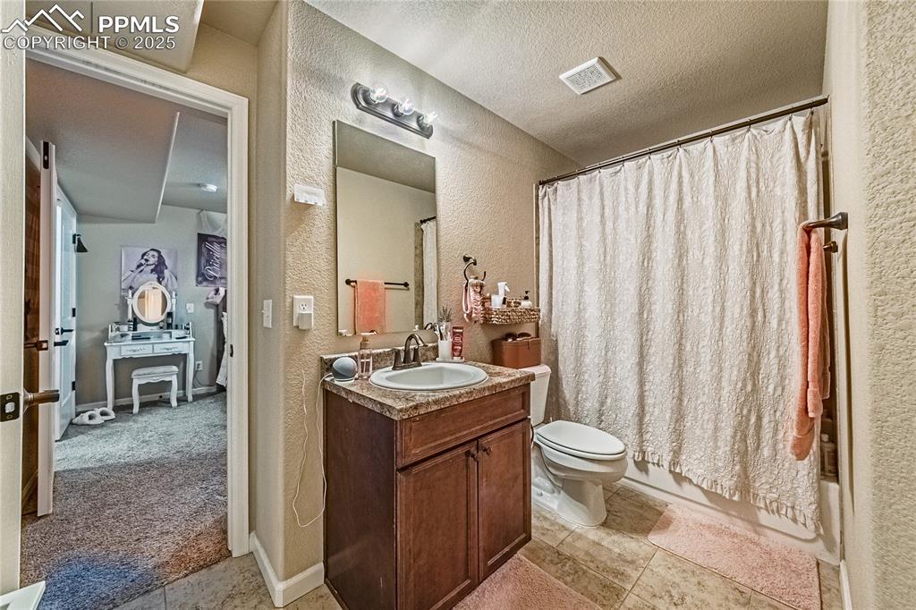 Full bath with a textured wall, vanity, shower / tub combo, a textured ceiling, and light tile patterned floors