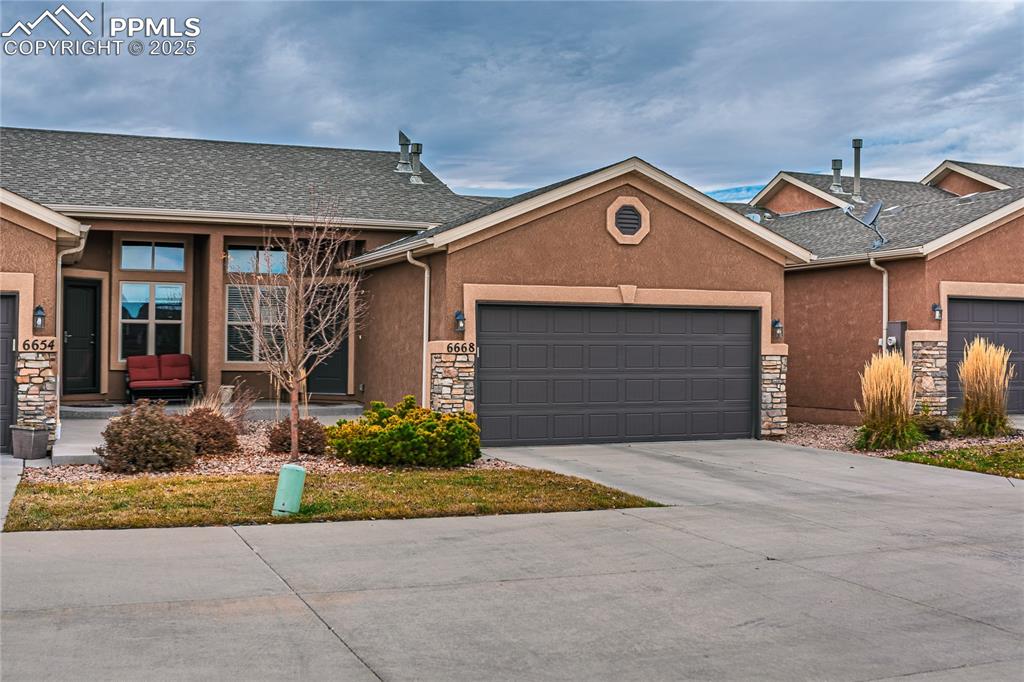Ranch-style home with stone siding, stucco siding, a garage, and concrete driveway
