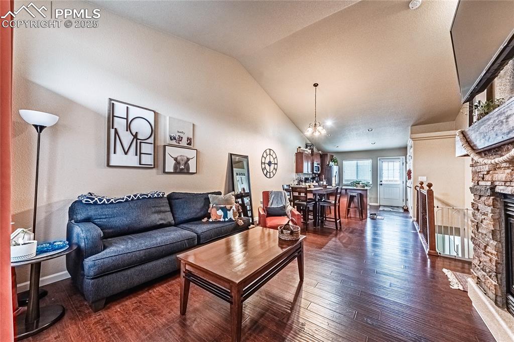 Living area featuring dark wood-type flooring, a stone fireplace, and high vaulted ceiling