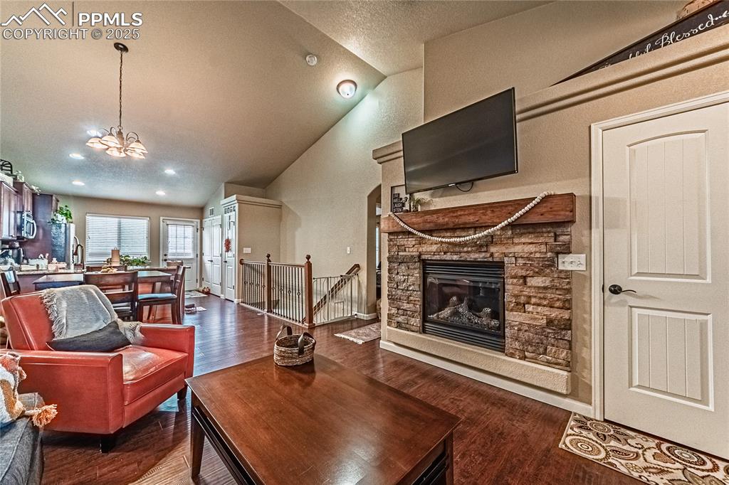 Living area with a stone fireplace, dark wood-type flooring, high vaulted ceiling, a textured ceiling, and a chandelier