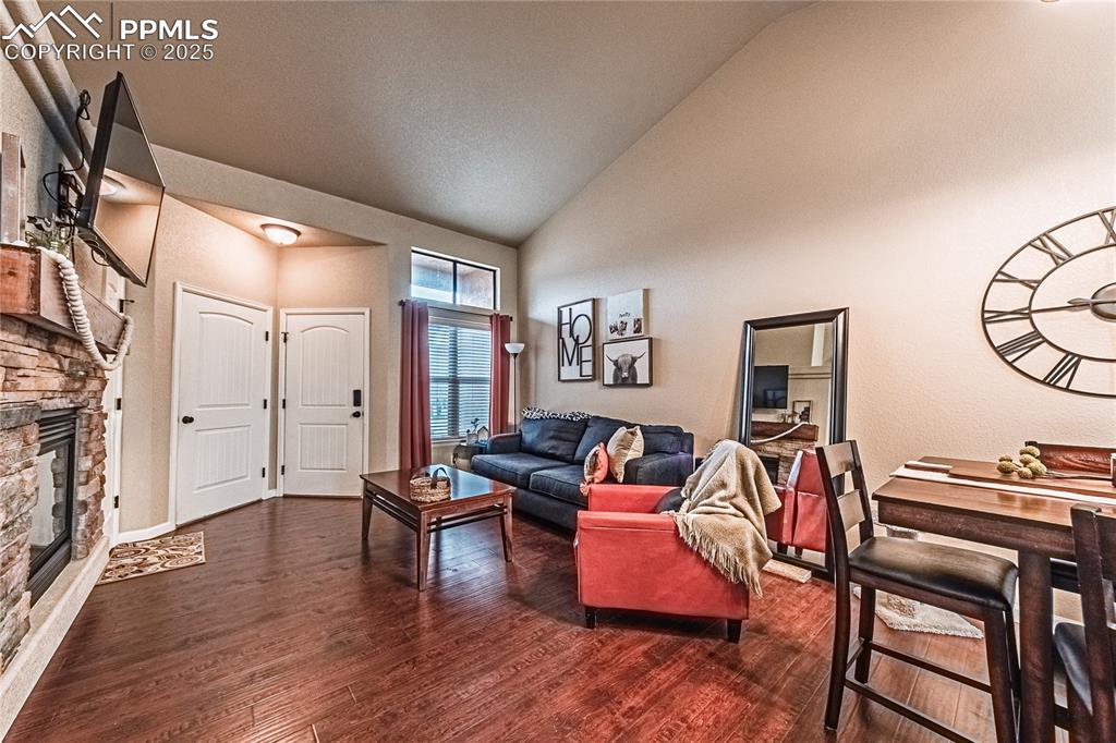 Living area featuring dark wood finished floors, a stone fireplace, and high vaulted ceiling