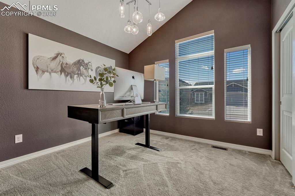 Main Level Bedroom #1 (currently being used as an office) has neutral carpet, a modern light fixture, designer paint tones, and a generous closet.
