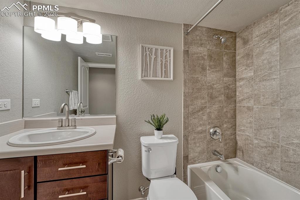 Basement Full Bathroom with comfort height vanity, mirror, and tiled tub/shower.
