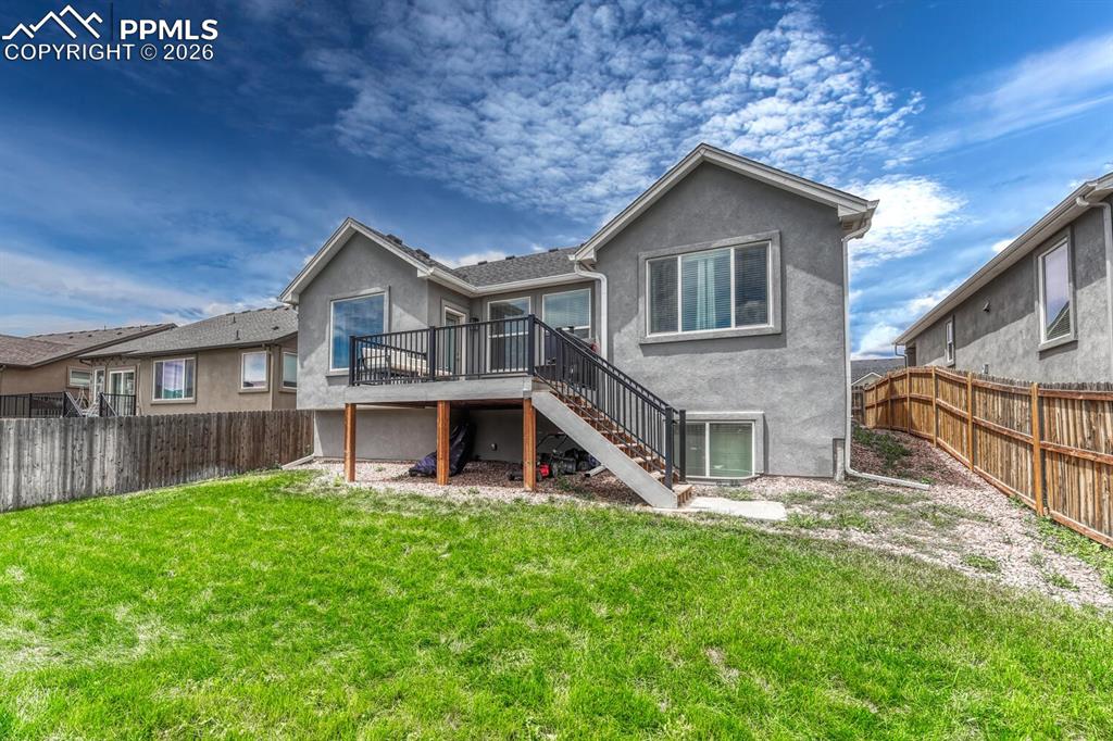 Rear view of home and fenced backyard with composite deck and stairs to the backyard.