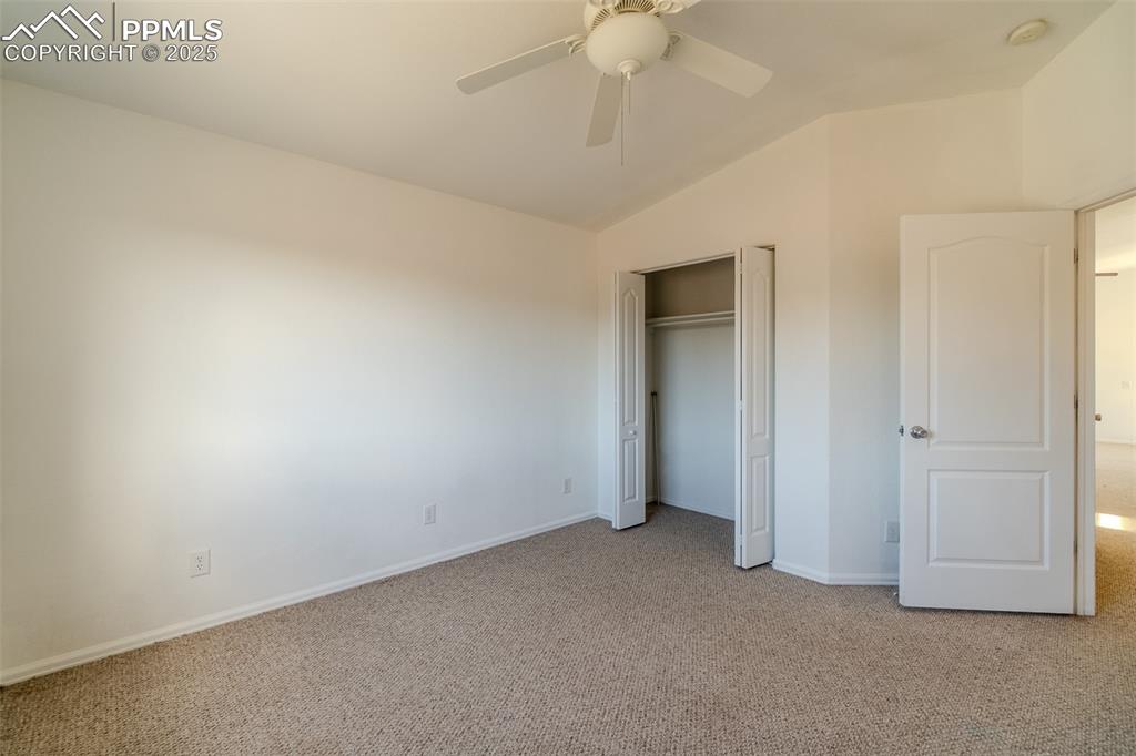 Unfurnished bedroom featuring carpet flooring, lofted ceiling, a closet, and ceiling fan