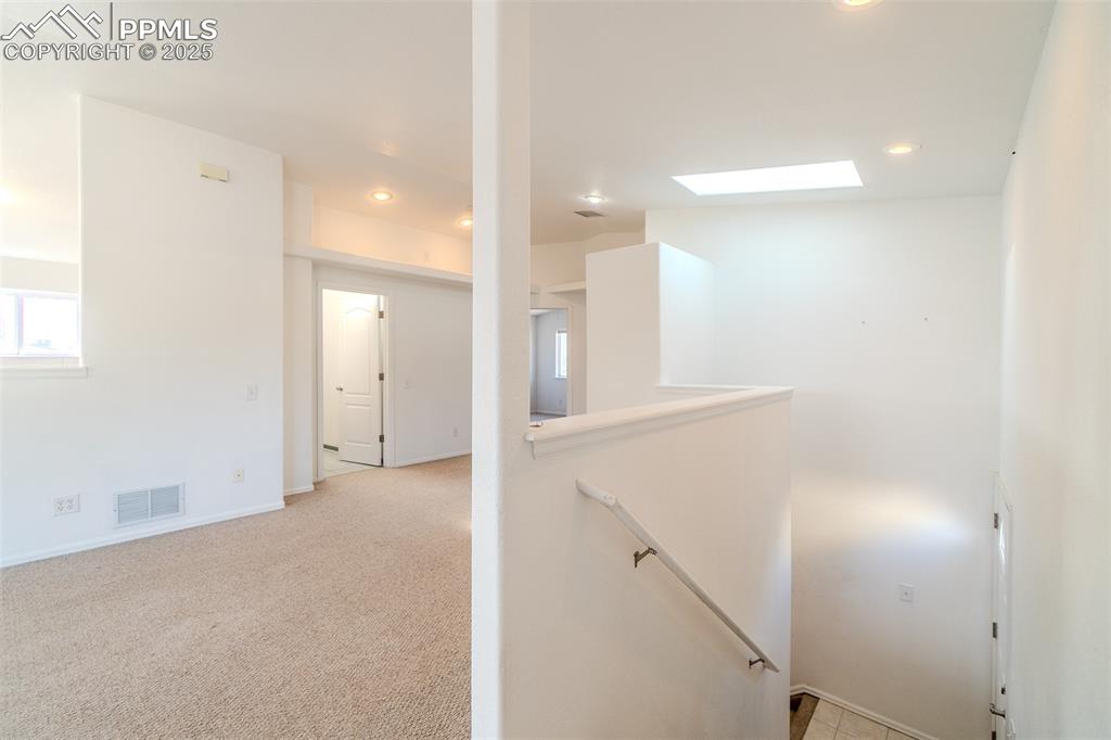Corridor with an upstairs landing, light colored carpet, recessed lighting, and a skylight