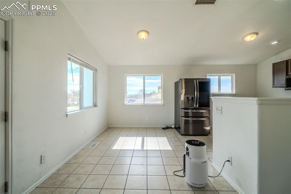 Kitchen with light tile patterned floors, stainless steel fridge, and vaulted ceiling