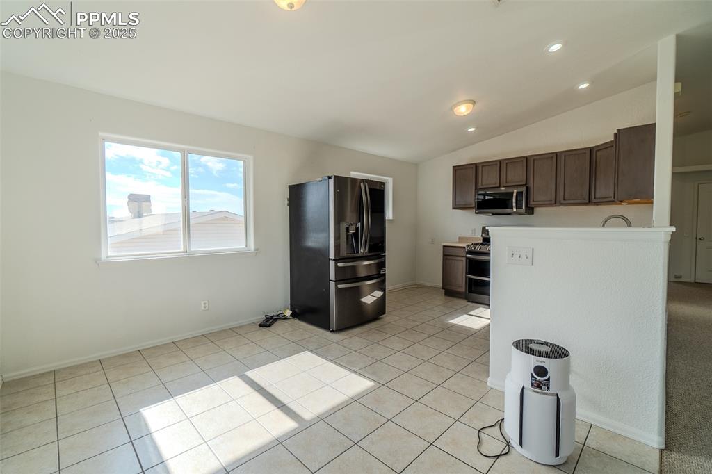 Kitchen featuring stainless steel appliances, light countertops, vaulted ceiling, light tile patterned floors, and recessed lighting