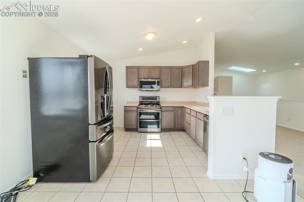 Kitchen with appliances with stainless steel finishes, light countertops, lofted ceiling, recessed lighting, and a skylight