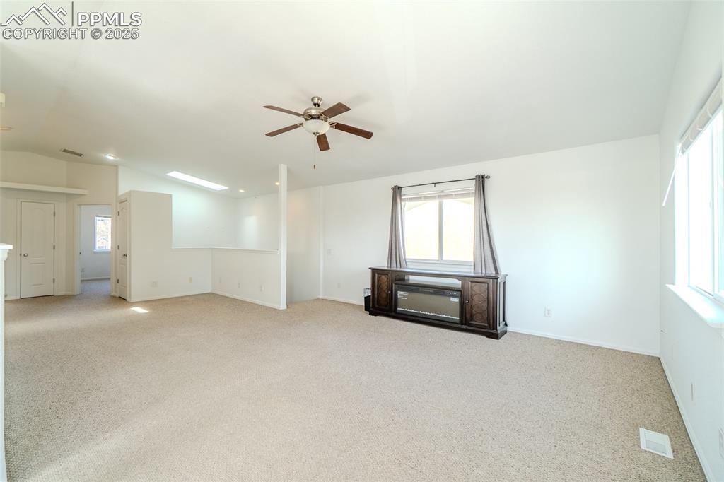 Unfurnished room with a skylight, light carpet, ceiling fan, and vaulted ceiling