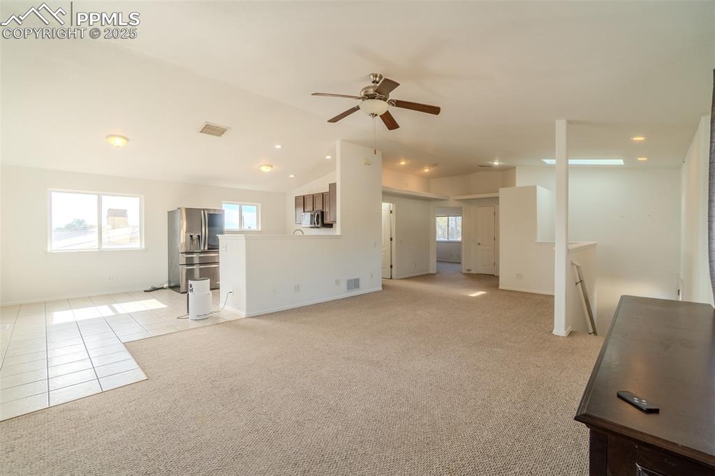 Unfurnished living room featuring vaulted ceiling, light tile patterned flooring, light carpet, ceiling fan, and recessed lighting