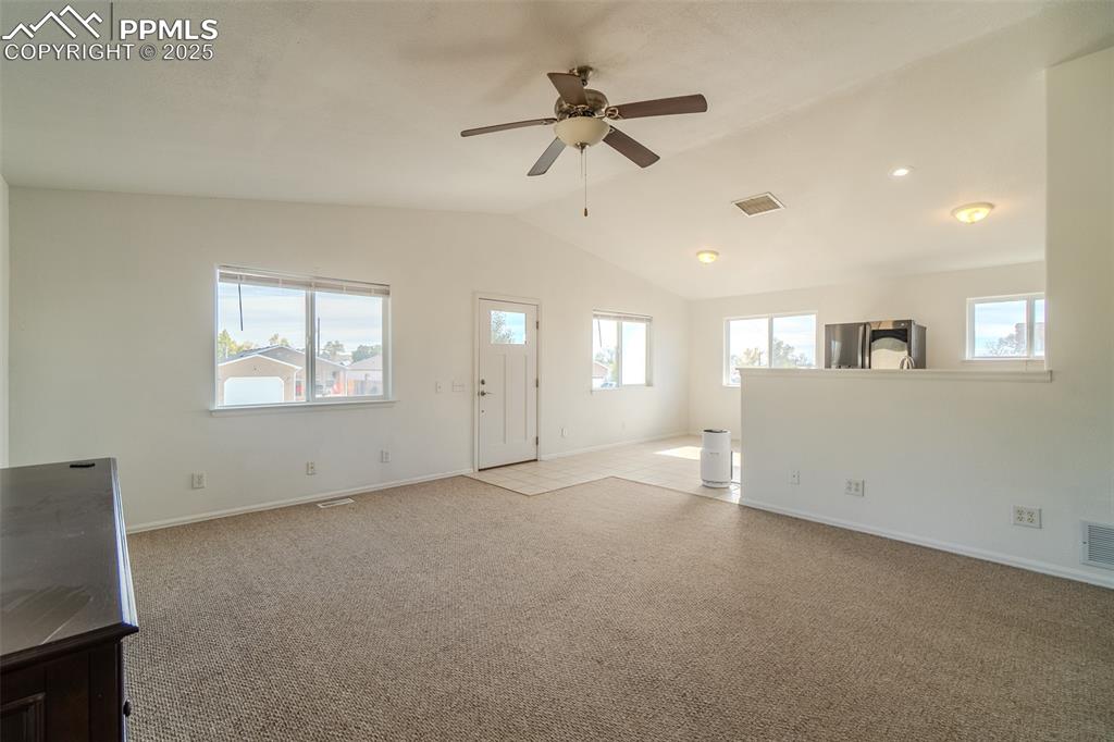 Unfurnished living room featuring light colored carpet, healthy amount of natural light, lofted ceiling, and ceiling fan