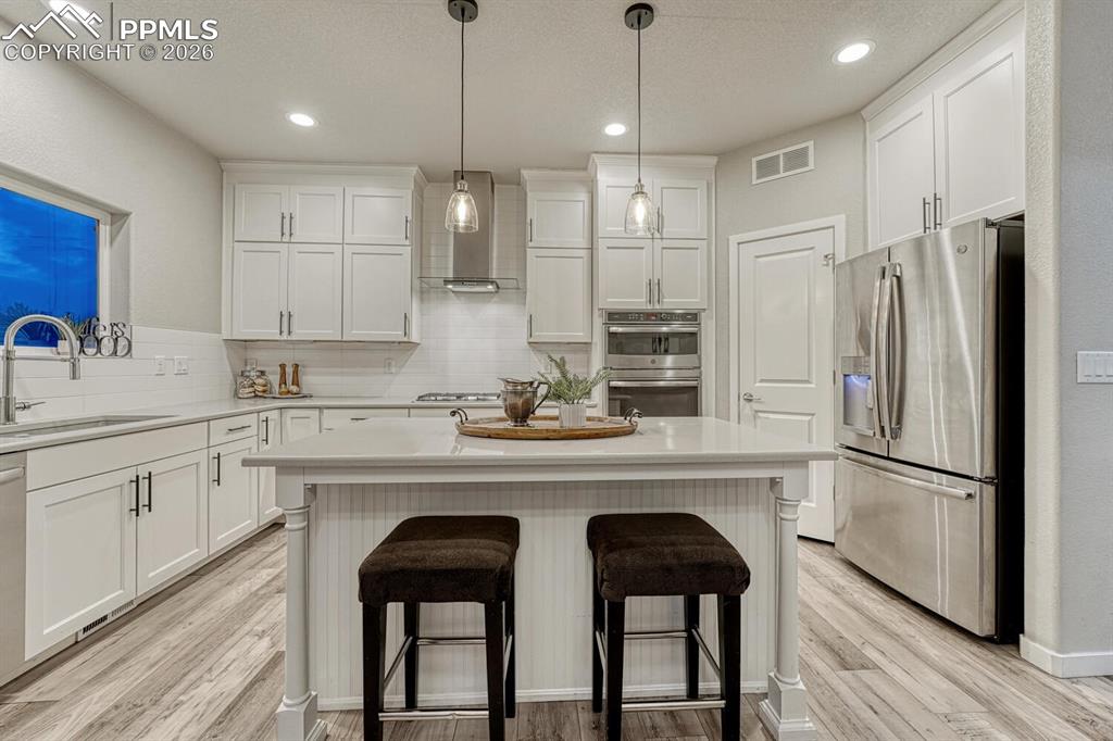 Sleek stainless steel appliances, pendant lighting fixtures, an integrated kitchen breakfast bar, white cabinetry, and a textured ceiling finish feature in this kitchen.